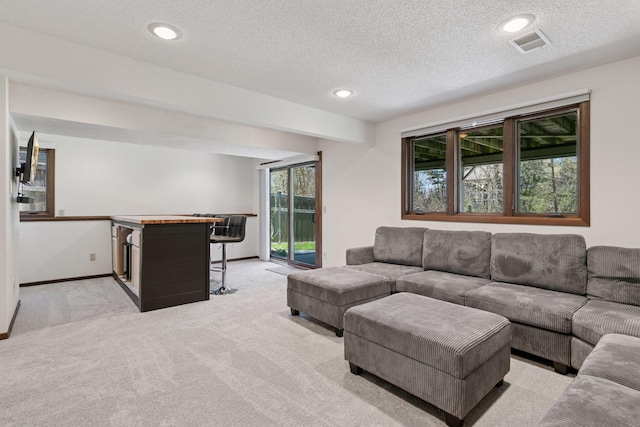 living area featuring visible vents, a textured ceiling, baseboards, and light colored carpet