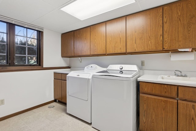 clothes washing area featuring cabinet space, baseboards, washing machine and dryer, and a sink