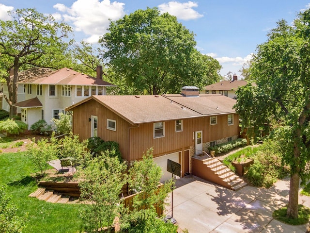 back of house with a shingled roof, an attached garage, driveway, and a chimney