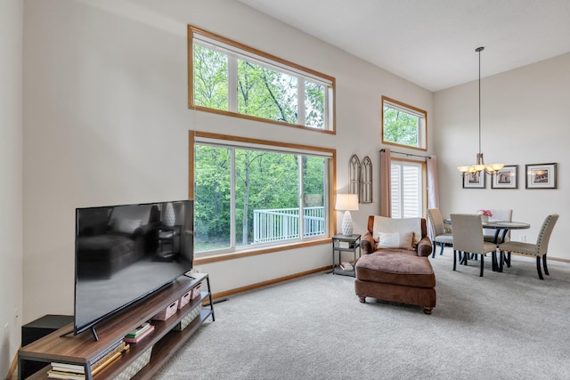 carpeted living area featuring a chandelier, a high ceiling, and baseboards