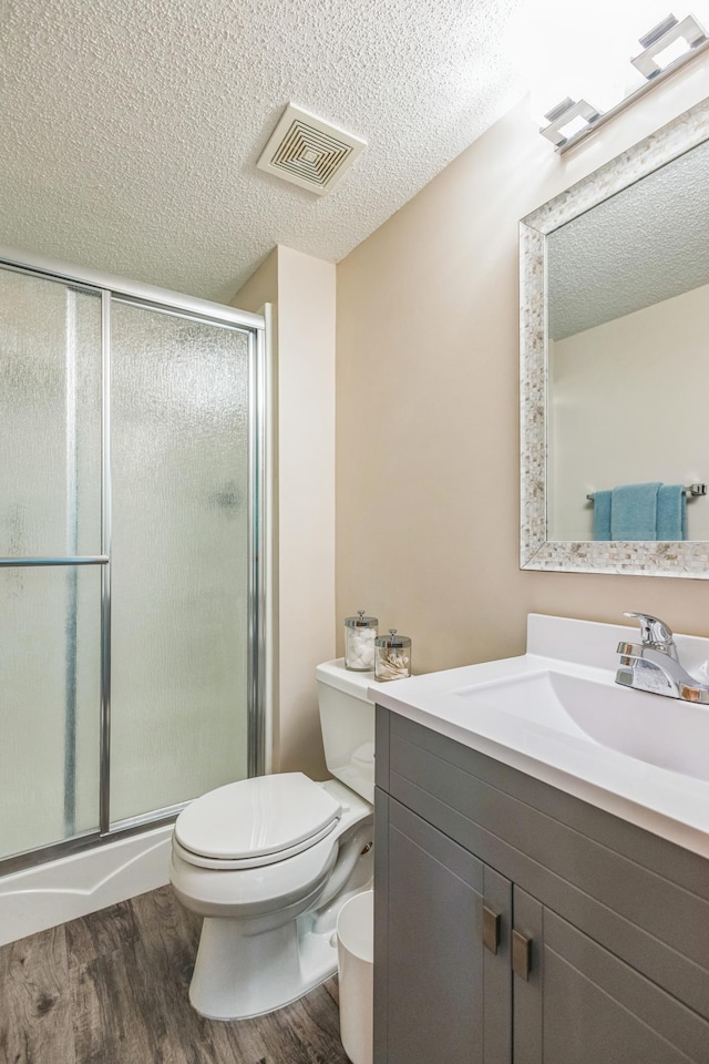 full bath with wood finished floors, toilet, a textured ceiling, a shower stall, and vanity