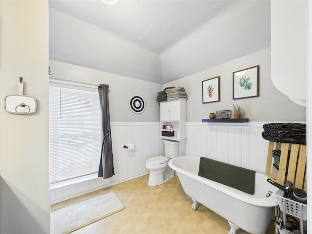 full bath featuring toilet, a wainscoted wall, tile patterned floors, a freestanding tub, and lofted ceiling