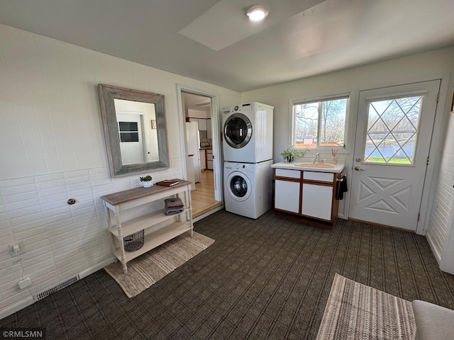 laundry area featuring dark colored carpet, visible vents, a sink, laundry area, and stacked washer / drying machine