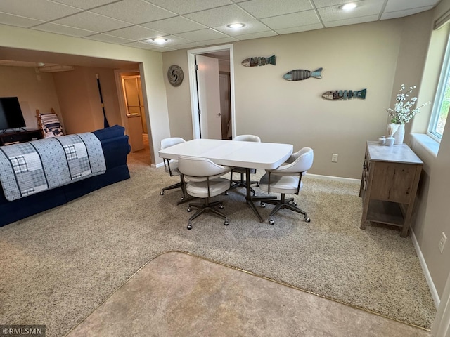 carpeted dining space featuring a paneled ceiling and baseboards