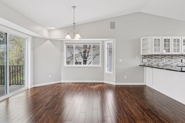 unfurnished dining area featuring dark wood-style flooring, an inviting chandelier, lofted ceiling, and visible vents