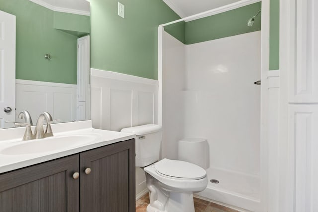 bathroom with wainscoting, a decorative wall, toilet, ornamental molding, and a stall shower