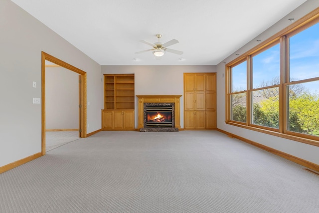 3088 Canyon Rd, Chaska, MN 55318 - unfurnished living room with a glass covered fireplace, baseboards, light colored carpet, built in shelves, and a ceiling fan