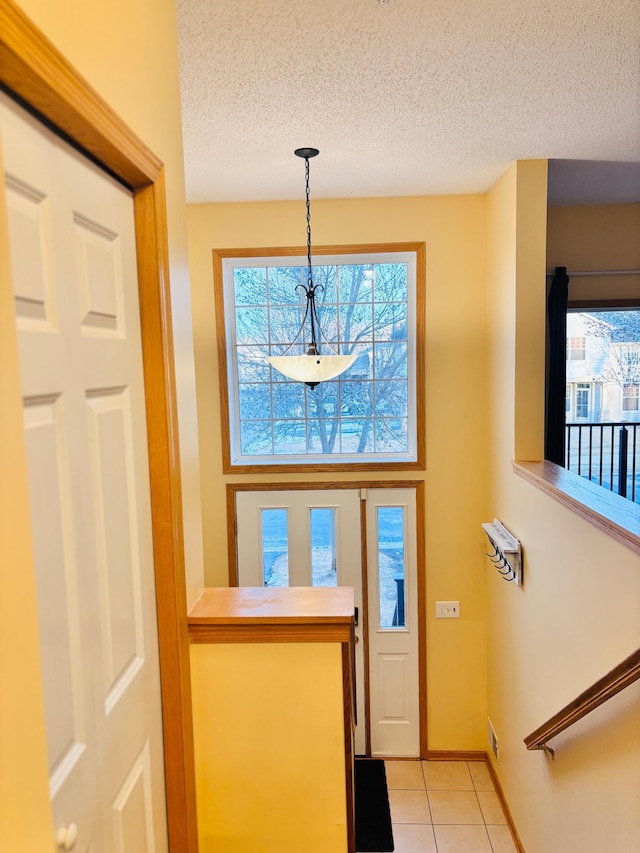 doorway featuring baseboards, a textured ceiling, plenty of natural light, and light tile patterned floors