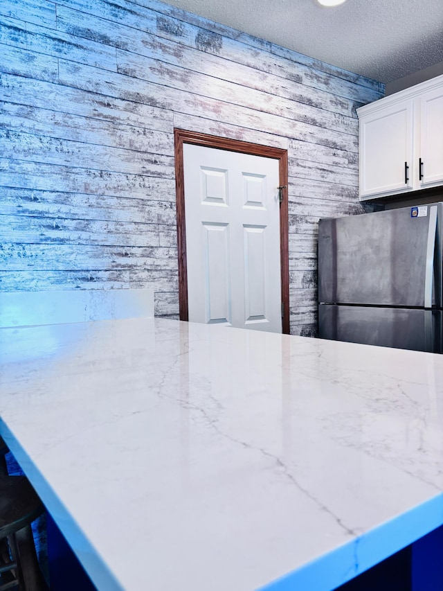 kitchen featuring freestanding refrigerator, wooden walls, a textured ceiling, white cabinets, and light stone counters