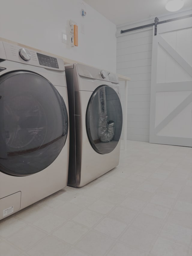 clothes washing area with light floors, a barn door, and washer and clothes dryer