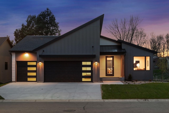 modern home featuring an attached garage, a standing seam roof, a lawn, driveway, and metal roof