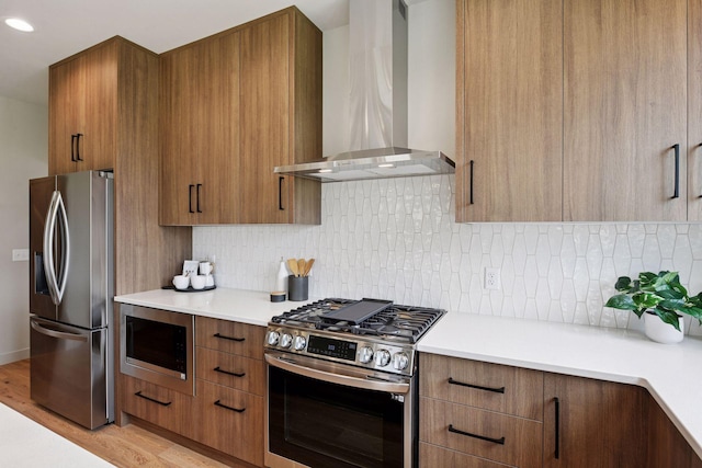 kitchen featuring wall chimney range hood, appliances with stainless steel finishes, brown cabinetry, and modern cabinets
