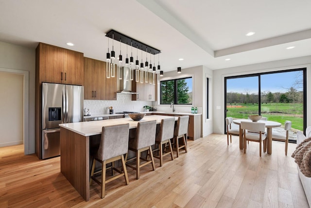 kitchen featuring brown cabinets, appliances with stainless steel finishes, light countertops, wall chimney exhaust hood, and a kitchen island