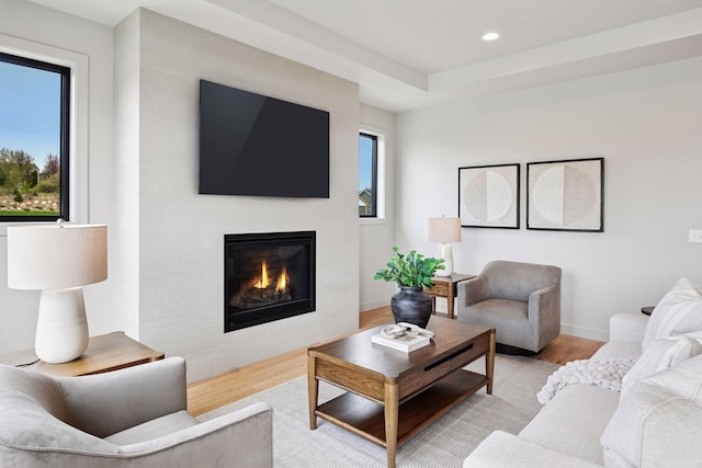 living room featuring a glass covered fireplace, baseboards, recessed lighting, and light wood-style flooring
