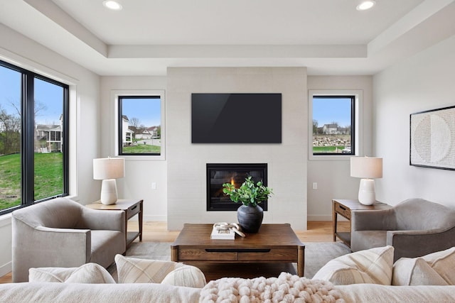 living area with a fireplace, light wood-style flooring, recessed lighting, baseboards, and a tray ceiling