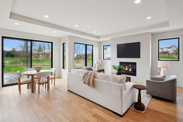 living room with recessed lighting, light wood-style flooring, a raised ceiling, and a large fireplace