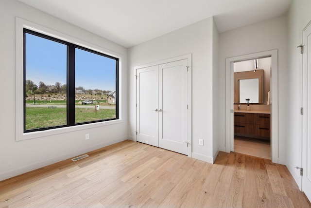 unfurnished bedroom with a sink, light wood-style flooring, baseboards, visible vents, and a closet