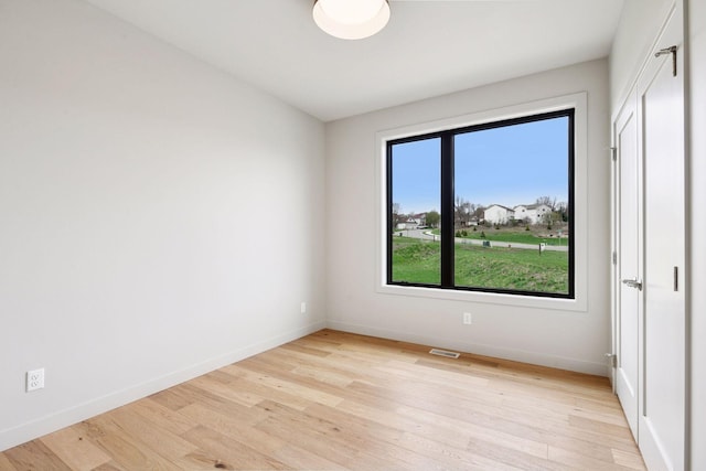 spare room with baseboards, light wood finished floors, and visible vents