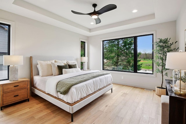 bedroom with visible vents, light wood-type flooring, baseboards, a tray ceiling, and recessed lighting