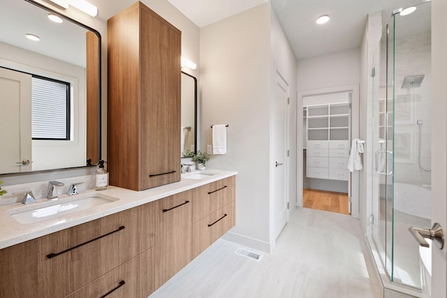full bathroom with a spacious closet, a shower stall, a sink, and visible vents