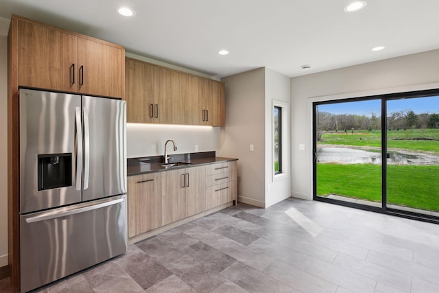 kitchen with dark countertops, stainless steel fridge, a sink, recessed lighting, and baseboards
