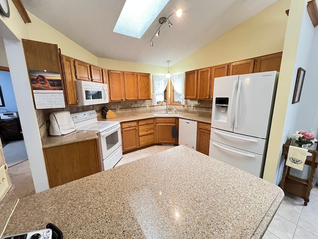 kitchen with a sink, brown cabinetry, white appliances, vaulted ceiling with skylight, and decorative backsplash
