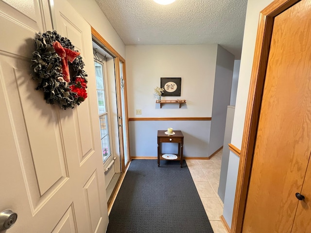 entryway with a textured ceiling, baseboards, and light tile patterned floors