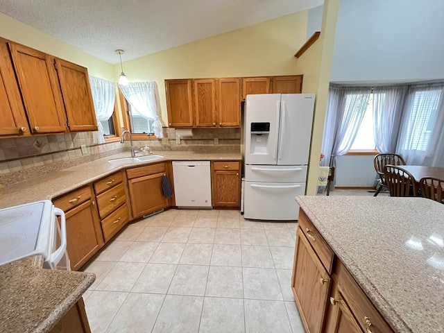 kitchen with brown cabinetry, white appliances, a sink, vaulted ceiling, and tasteful backsplash