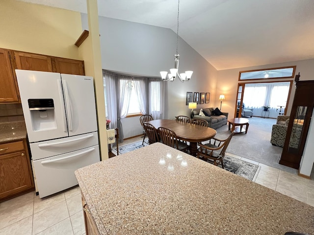 kitchen with brown cabinetry, light tile patterned flooring, high vaulted ceiling, white refrigerator with ice dispenser, and a notable chandelier