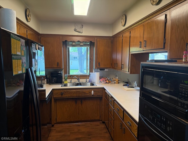 kitchen featuring black appliances, a sink, light countertops, dark wood-type flooring, and brown cabinets