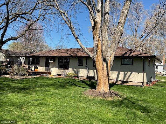 back of house with stucco siding, a yard, and roof with shingles