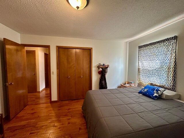bedroom with a textured ceiling, wood finished floors, and a closet