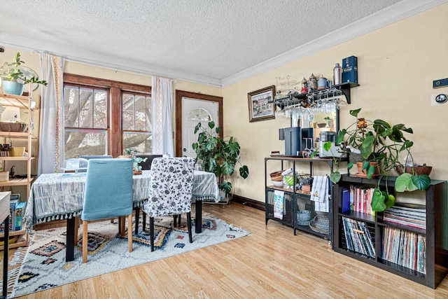 dining room with crown molding, baseboards, a textured ceiling, and wood finished floors