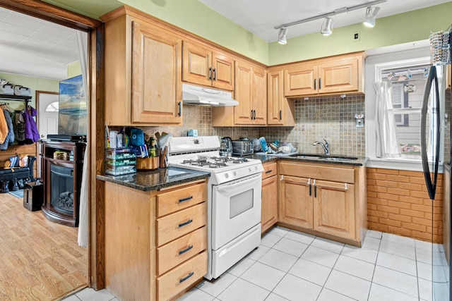 kitchen featuring decorative backsplash, light brown cabinetry, gas range gas stove, a sink, and under cabinet range hood