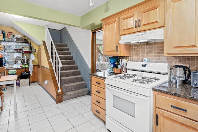 kitchen with light brown cabinetry, white gas stove, light tile patterned floors, tasteful backsplash, and under cabinet range hood