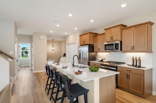 6758 Wildflower Way, Minnetrista, MN 55331 - kitchen featuring stainless steel appliances, a sink, a center island with sink, light wood-type flooring, and tasteful backsplash