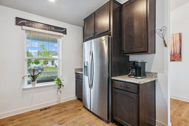 kitchen featuring stainless steel fridge with ice dispenser, dark brown cabinets, light wood-style flooring, baseboards, and light stone countertops