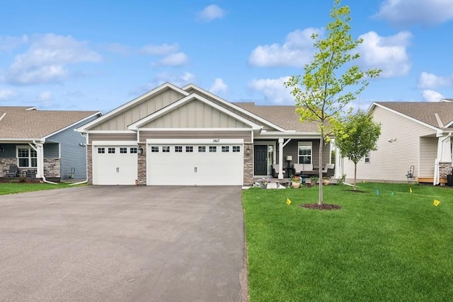 craftsman-style house featuring board and batten siding, driveway, a front yard, a garage, and stone siding