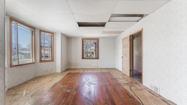 empty room featuring wood-type flooring, visible vents, plenty of natural light, and a drop ceiling