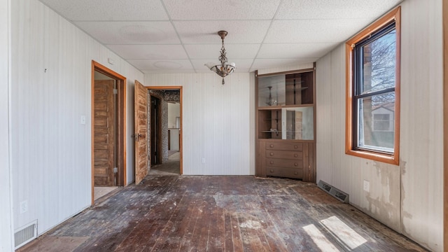 unfurnished dining area with wood-type flooring, wood walls, visible vents, and a drop ceiling