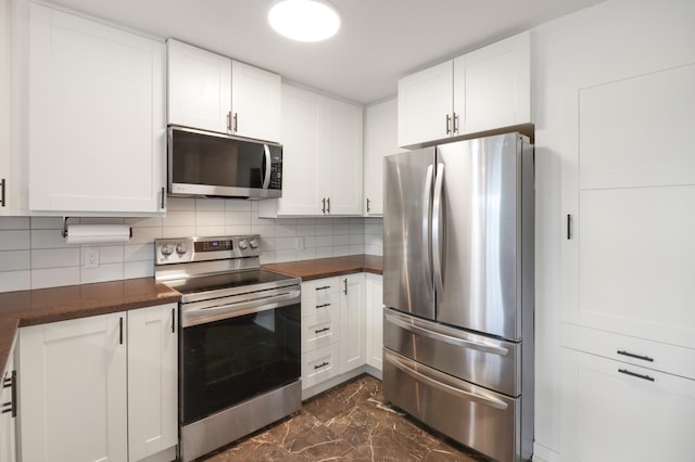 kitchen featuring dark countertops, appliances with stainless steel finishes, white cabinetry, and marble finish floor