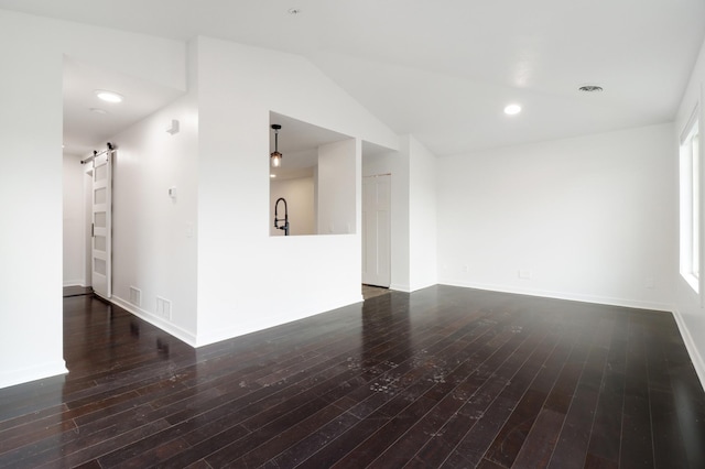 unfurnished living room featuring baseboards, a barn door, lofted ceiling, and hardwood / wood-style flooring