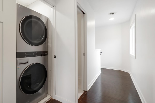 washroom featuring laundry area, dark wood-style flooring, stacked washer / dryer, visible vents, and baseboards