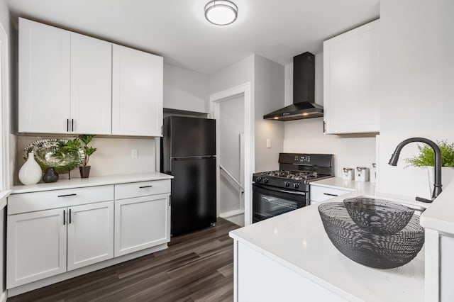 kitchen with wall chimney range hood, light countertops, white cabinets, black appliances, and dark wood-style floors