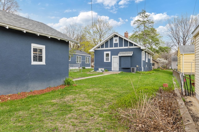 back of house with a lawn, central AC unit, stucco siding, and a chimney