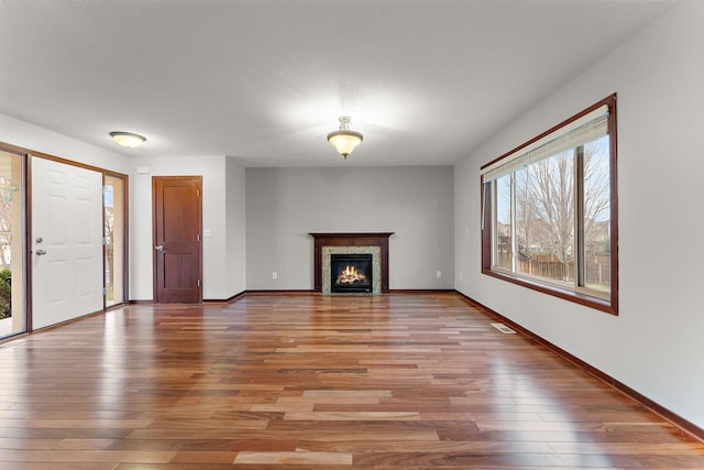 unfurnished living room with baseboards, a glass covered fireplace, wood finished floors, and visible vents
