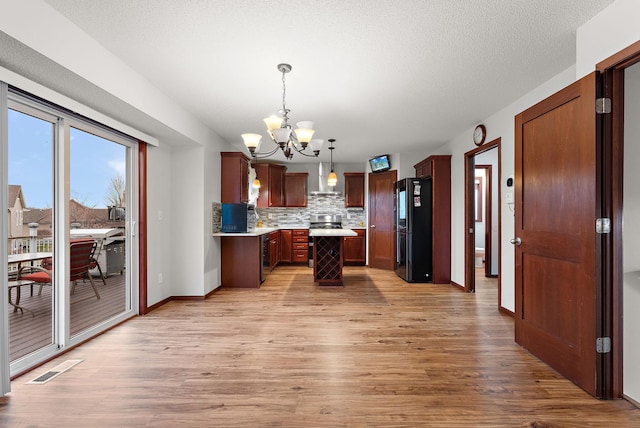 kitchen with freestanding refrigerator, light wood-style floors, light countertops, wall chimney exhaust hood, and a notable chandelier