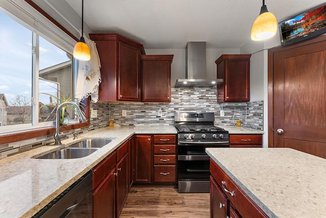 kitchen with wood finished floors, wall chimney range hood, reddish brown cabinets, a sink, and appliances with stainless steel finishes
