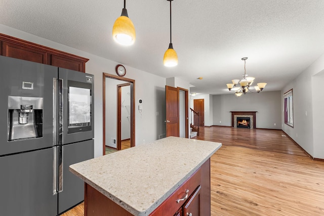 kitchen with a kitchen island, light countertops, stainless steel fridge with ice dispenser, a notable chandelier, and light wood-style flooring
