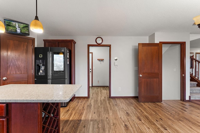 kitchen featuring a kitchen breakfast bar, decorative light fixtures, light countertops, light wood finished floors, and black refrigerator with ice dispenser